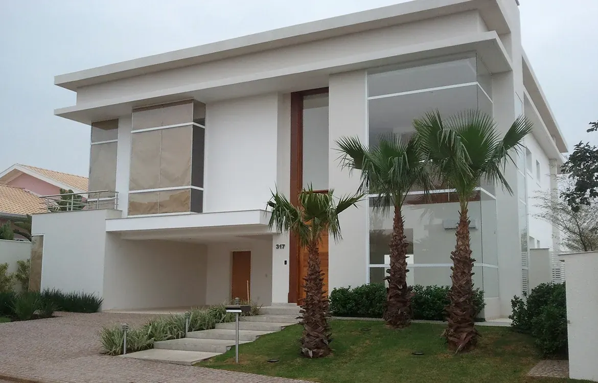 Residência contemporânea de fachada branca com palmeiras em Alphaville